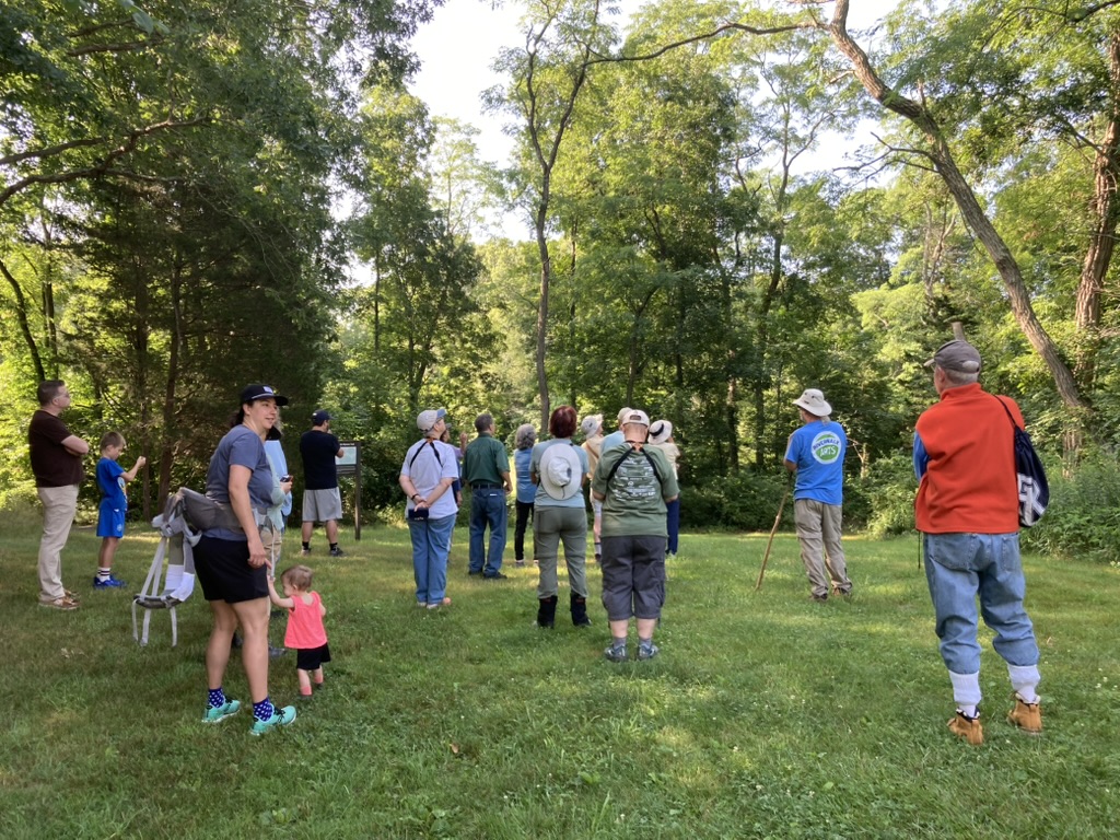 Group of people in summer clothes standing near trees.